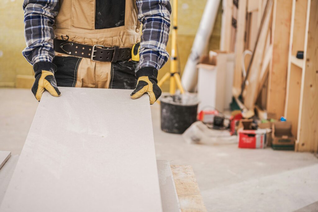 Male Contractor Holding Piece Of Drywall Material.