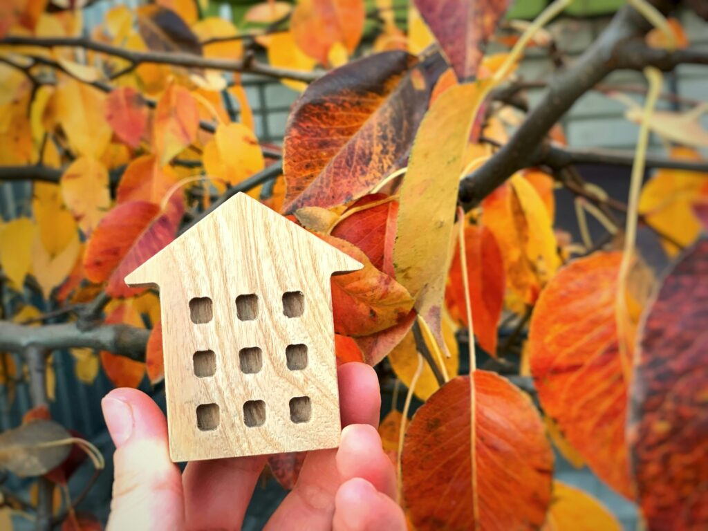 Miniature wooden house in hands on a background of autumn leaves